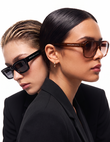 Two women in black outfits wearing Waylon Smith sunglasses, one in black square frames and one in tortoiseshell frames
